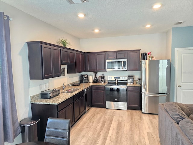 604 Madison Dr, Davenport, FL 33837 - kitchen featuring appliances with stainless steel finishes, dark brown cabinetry, light wood-style floors, light stone counters, and a textured ceiling
