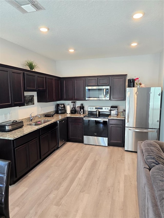 kitchen with dark brown cabinets, light wood-type flooring, sink, and appliances with stainless steel finishes