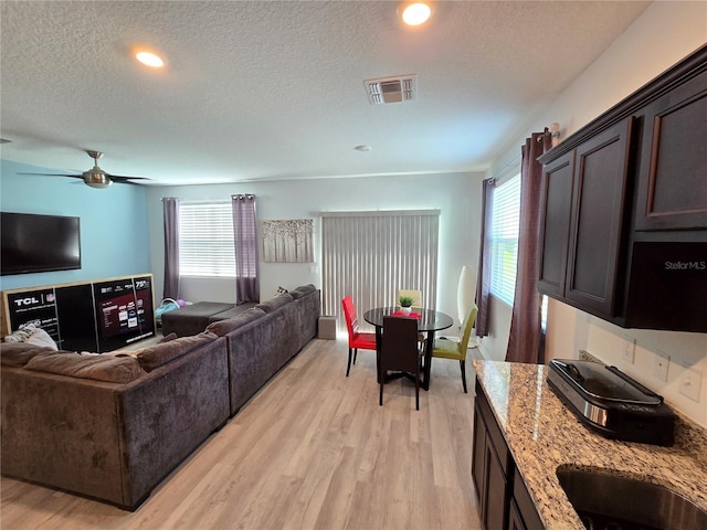 living room with ceiling fan, light hardwood / wood-style floors, and a textured ceiling