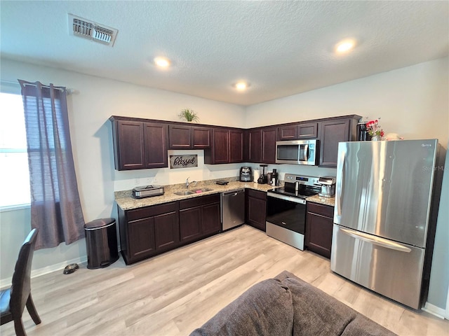 kitchen featuring sink, stainless steel appliances, light hardwood / wood-style flooring, a textured ceiling, and dark brown cabinets