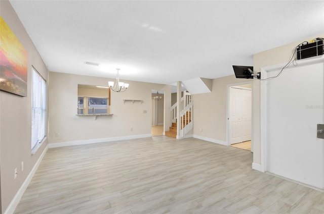 interior space with an inviting chandelier, light wood finished floors, baseboards, visible vents, and stairway