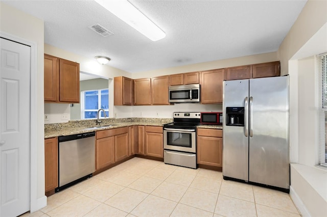kitchen featuring visible vents, light stone countertops, brown cabinets, a sink, and appliances with stainless steel finishes