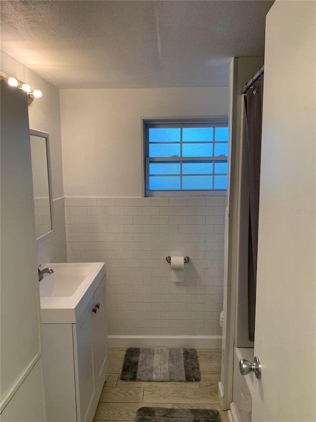 bathroom featuring vanity, hardwood / wood-style floors, a textured ceiling, and tile walls