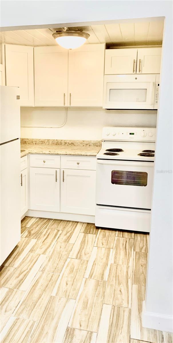 kitchen with white appliances, white cabinetry, wooden ceiling, and light stone counters