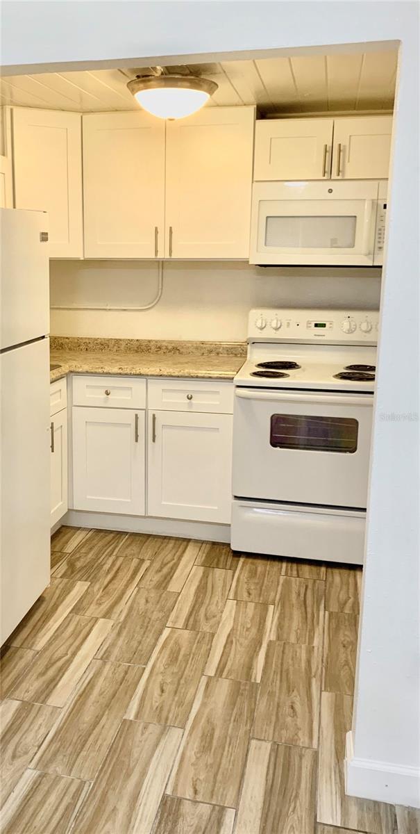 kitchen with white cabinetry, wooden ceiling, white appliances, and light wood-type flooring