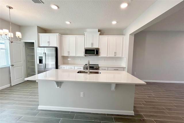 kitchen featuring sink, appliances with stainless steel finishes, an island with sink, pendant lighting, and white cabinets