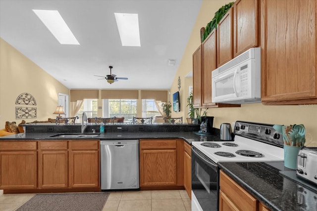 kitchen featuring light tile patterned flooring, white appliances, dark stone counters, and sink