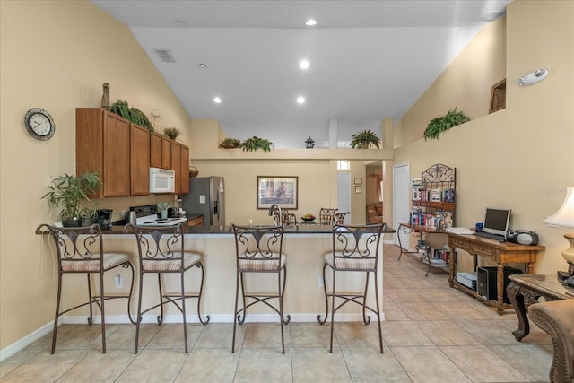 kitchen featuring a breakfast bar, white appliances, lofted ceiling, light tile patterned floors, and kitchen peninsula