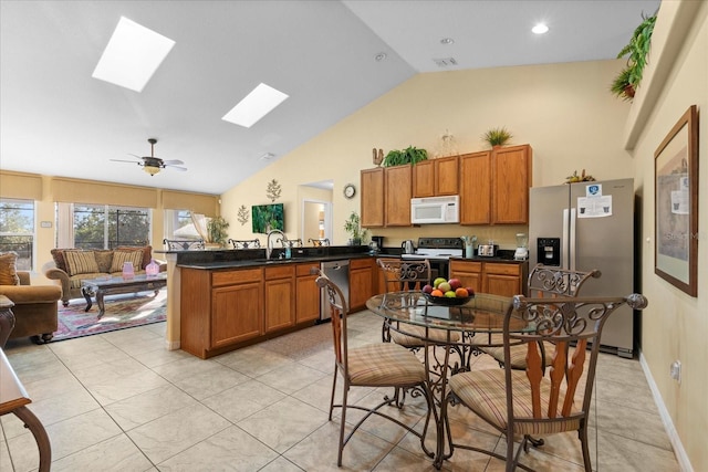 kitchen featuring kitchen peninsula, a skylight, stainless steel appliances, ceiling fan, and high vaulted ceiling