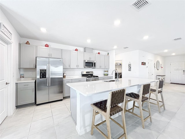 kitchen with sink, a kitchen breakfast bar, gray cabinets, a center island with sink, and appliances with stainless steel finishes