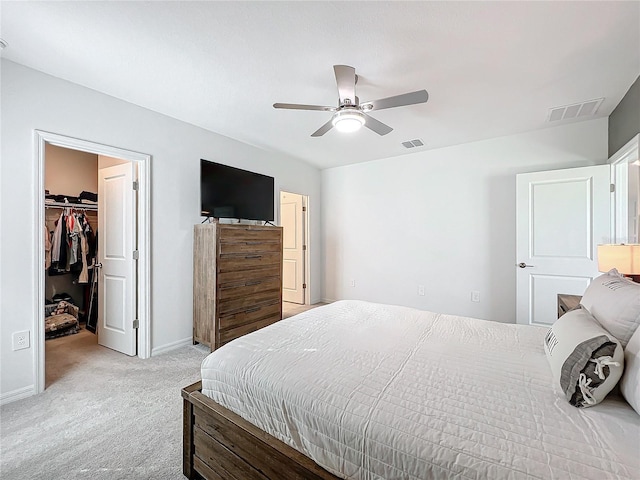 bedroom with a walk in closet, ceiling fan, a closet, and light carpet