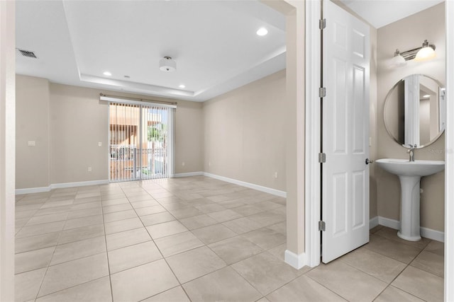 empty room featuring a tray ceiling, sink, and light tile patterned floors