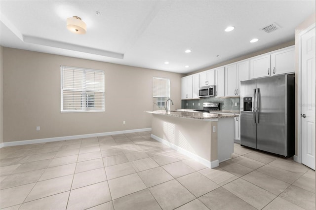 kitchen featuring white cabinetry, tasteful backsplash, an island with sink, stainless steel appliances, and light stone countertops