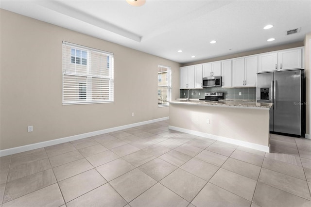 kitchen with appliances with stainless steel finishes, light stone counters, an island with sink, white cabinets, and decorative backsplash