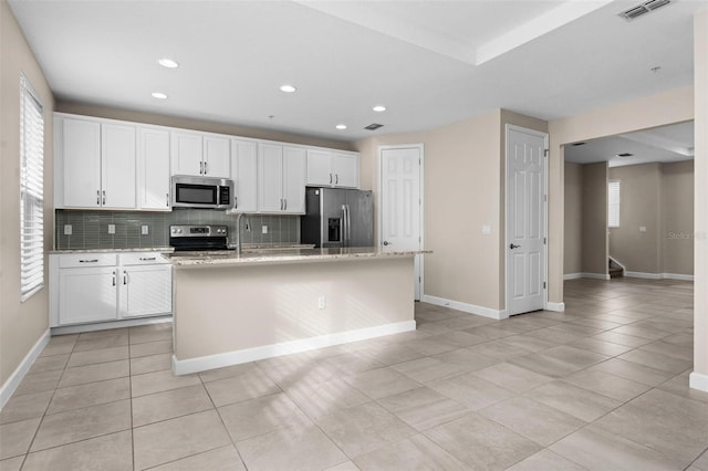 kitchen featuring appliances with stainless steel finishes, tasteful backsplash, white cabinetry, plenty of natural light, and a center island with sink