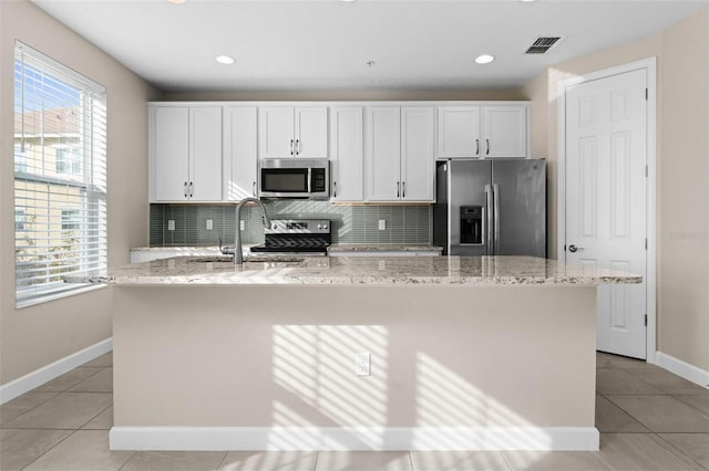 kitchen featuring a center island with sink, light stone countertops, white cabinets, and appliances with stainless steel finishes