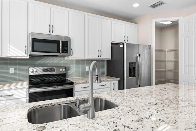 kitchen featuring sink, light stone counters, stainless steel appliances, decorative backsplash, and white cabinets