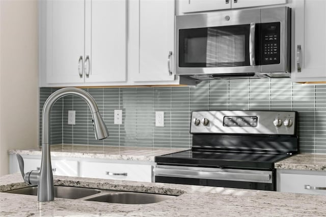 kitchen with sink, light stone counters, white cabinets, stainless steel appliances, and backsplash