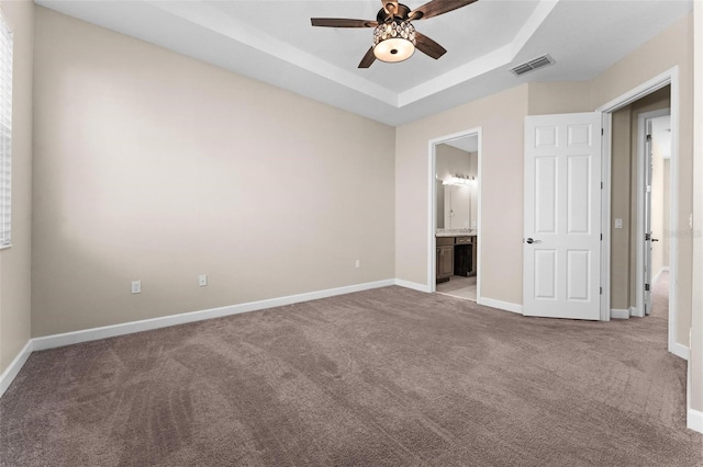 unfurnished bedroom featuring ceiling fan, ensuite bath, a tray ceiling, and light carpet