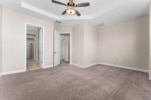 unfurnished bedroom with ceiling fan, a tray ceiling, and light carpet