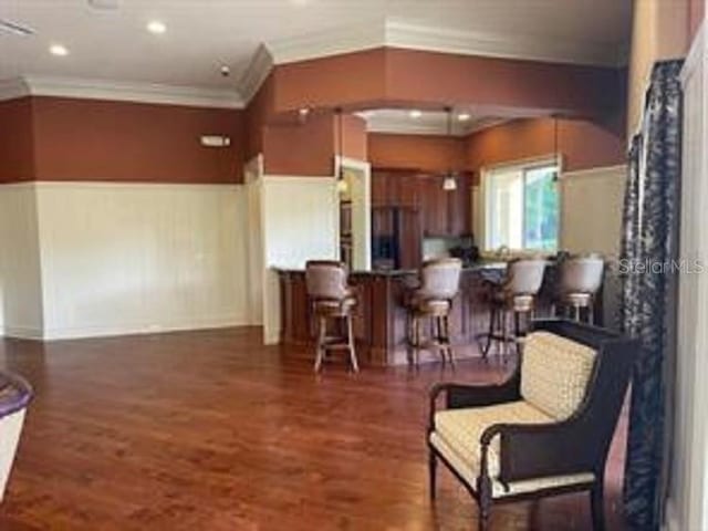 interior space with dark wood-type flooring, ornamental molding, and a breakfast bar