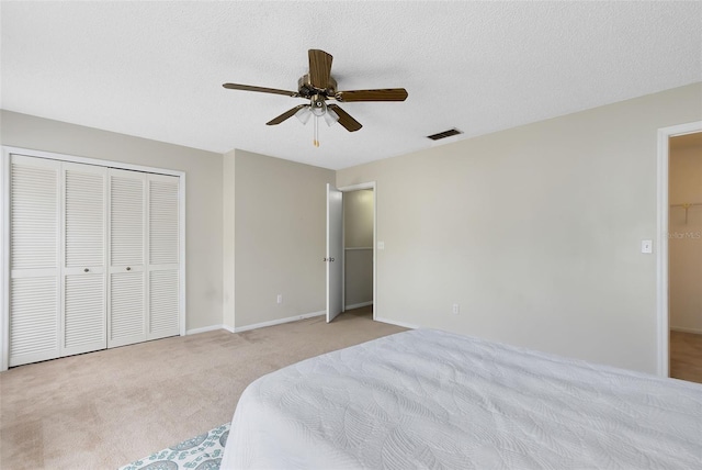 bedroom featuring ceiling fan, light colored carpet, a closet, and a textured ceiling