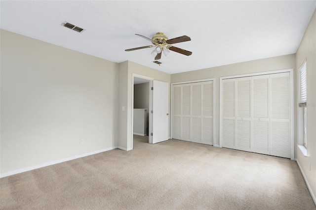 unfurnished bedroom featuring ceiling fan, two closets, and light carpet