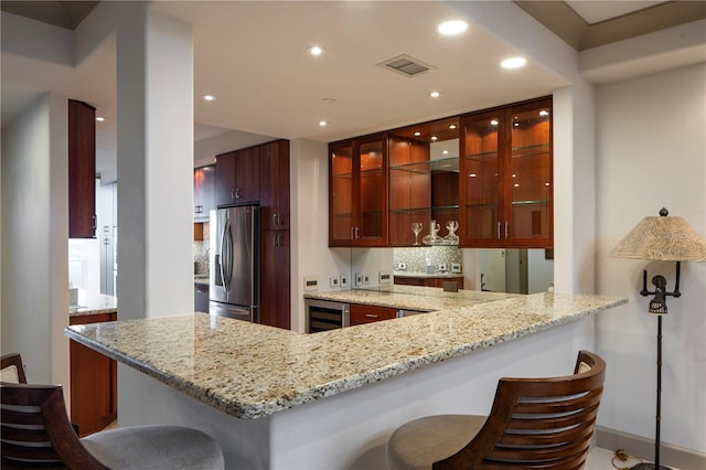 kitchen featuring kitchen peninsula, light stone counters, beverage cooler, stainless steel fridge with ice dispenser, and a breakfast bar area