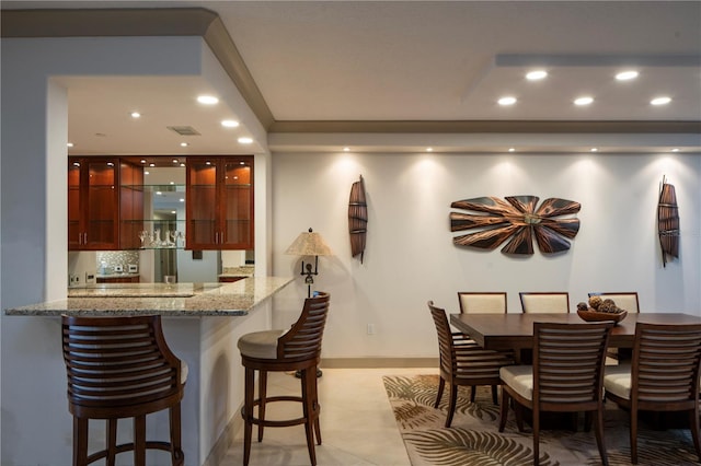 interior space with tasteful backsplash, light stone counters, kitchen peninsula, a breakfast bar, and light tile patterned floors