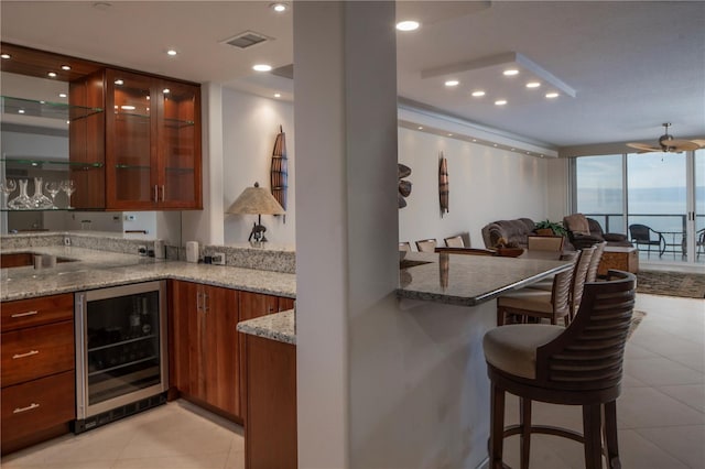 kitchen featuring floor to ceiling windows, a kitchen breakfast bar, wine cooler, light stone counters, and kitchen peninsula