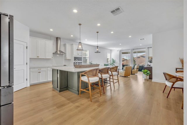 kitchen with a breakfast bar, a kitchen island with sink, white cabinets, hanging light fixtures, and wall chimney exhaust hood