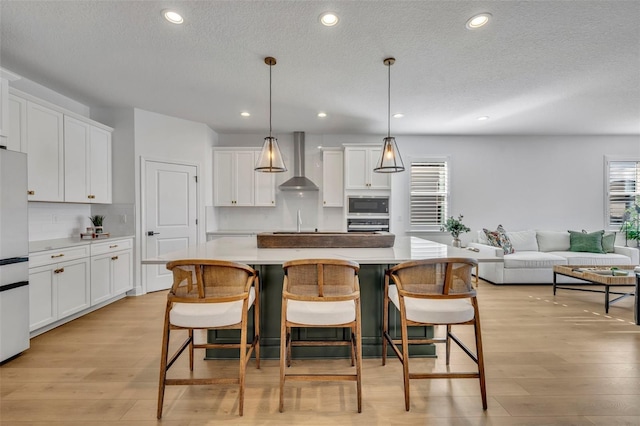 kitchen featuring built in microwave, a center island, wall chimney exhaust hood, pendant lighting, and white cabinets