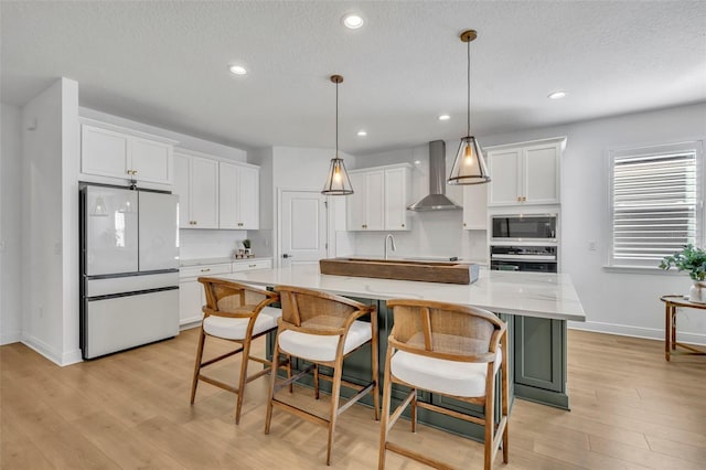 kitchen featuring white cabinetry, a spacious island, wall chimney range hood, and appliances with stainless steel finishes