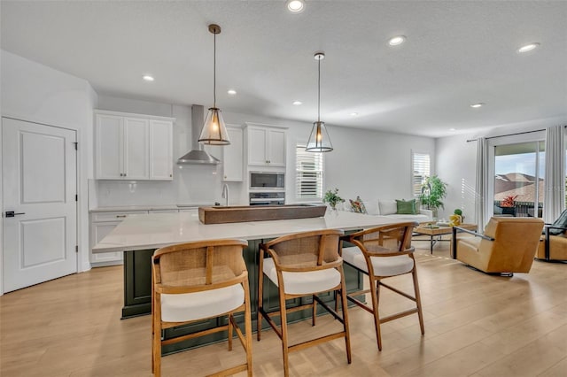 kitchen featuring a large island, wall chimney exhaust hood, a kitchen bar, and white cabinetry