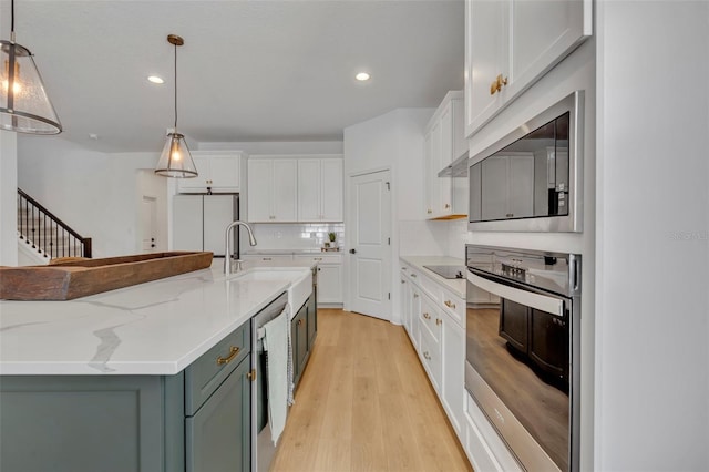 kitchen with stainless steel oven, tasteful backsplash, an island with sink, decorative light fixtures, and white cabinets