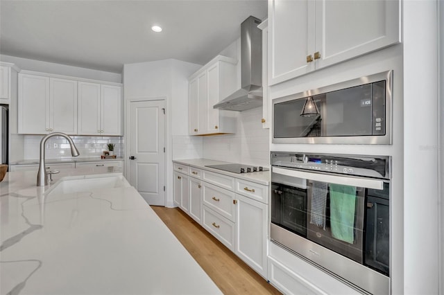 kitchen with white cabinets, wall chimney exhaust hood, stainless steel oven, and sink