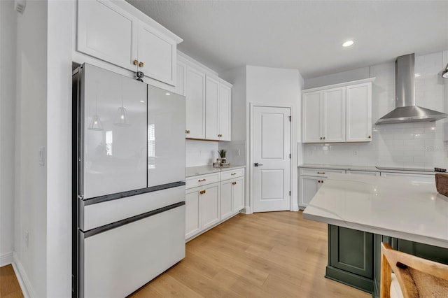 kitchen featuring backsplash, white cabinets, wall chimney exhaust hood, light hardwood / wood-style floors, and white fridge