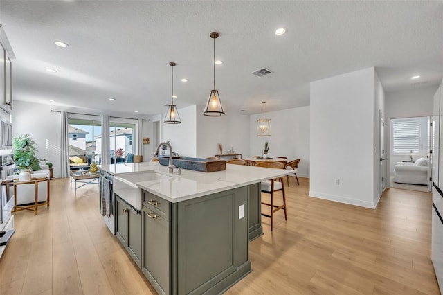 kitchen with light stone countertops, sink, hanging light fixtures, a kitchen island with sink, and light wood-type flooring