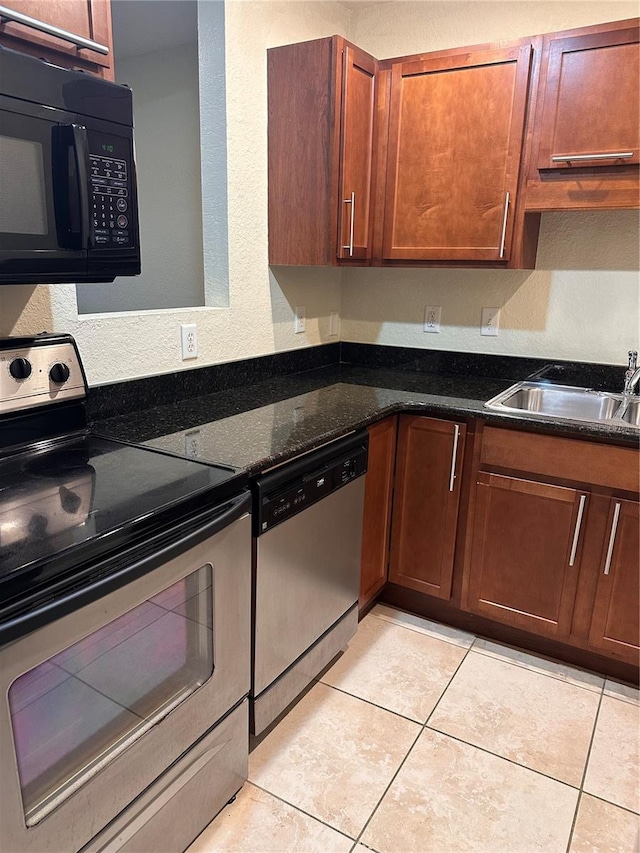 kitchen with light tile patterned floors, stainless steel appliances, dark stone counters, and sink