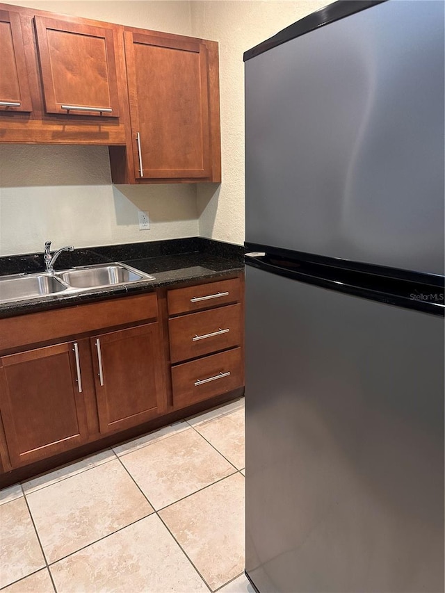 kitchen with light tile patterned flooring, stainless steel refrigerator, dark stone counters, and sink