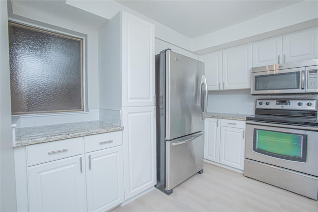 kitchen with white cabinets, appliances with stainless steel finishes, light wood-type flooring, and light stone countertops