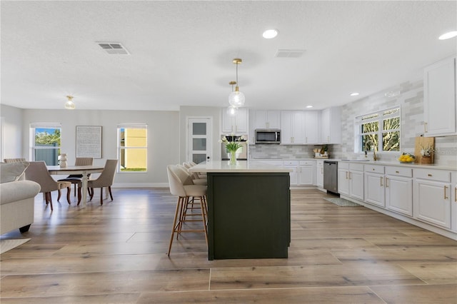 kitchen featuring decorative light fixtures, a breakfast bar area, white cabinets, a center island, and stainless steel appliances