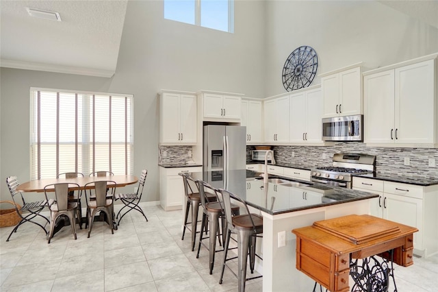 kitchen with light tile patterned flooring, a breakfast bar, stainless steel appliances, white cabinets, and an island with sink