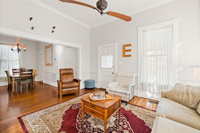 living room with ornamental molding, ceiling fan with notable chandelier, and wood-type flooring