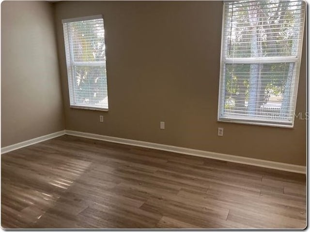 empty room with dark hardwood / wood-style floors and plenty of natural light