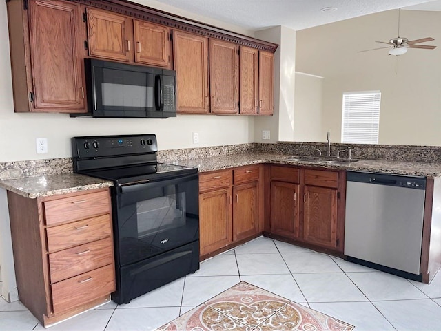 kitchen with light tile patterned floors, a sink, dark stone counters, black appliances, and brown cabinetry