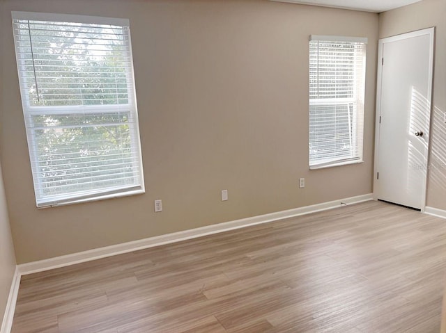 empty room featuring light wood-type flooring, plenty of natural light, and baseboards