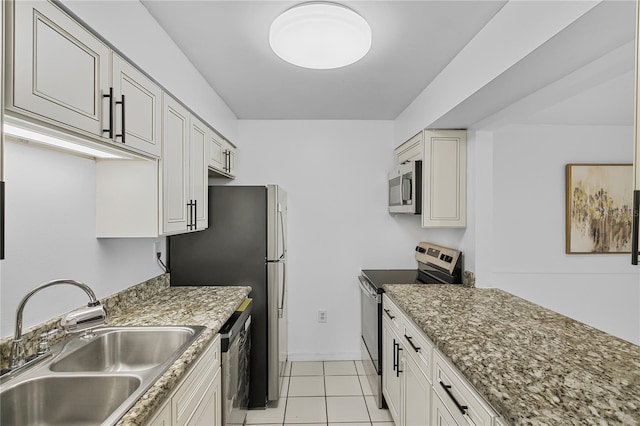 kitchen with light tile patterned floors, baseboards, light stone counters, stainless steel appliances, and a sink