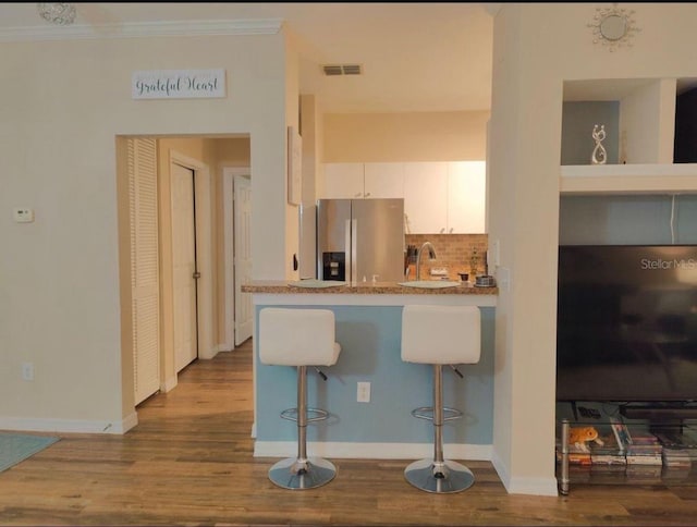 kitchen with light stone countertops, stainless steel fridge, light hardwood / wood-style floors, a breakfast bar area, and white cabinets