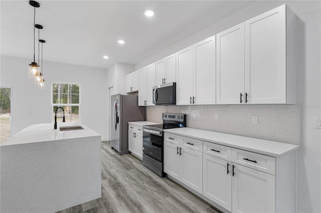 kitchen with stainless steel appliances, sink, light hardwood / wood-style flooring, white cabinets, and hanging light fixtures